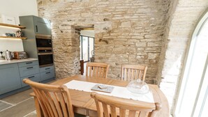 A rustic stone wall interior with a wooden dining table and chairs, a kitchen with modern appliances, and a view through a window. - West Dunkirk Hemmels (Hexham)