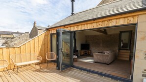 A wooden deck with a glass door leading to an interior space with a sofa, a television, and a fireplace. - West Dunkirk Hemmels (Hexham)