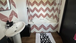A bathroom with a white sink, a bathtub, and a shower. The walls have a geometric tile pattern. - Cosy Chichester Apartment (Chichester)