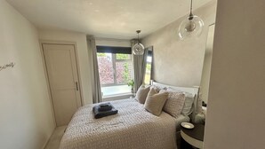 A bedroom with a bed, a nightstand, a window with curtains, and a ceiling light fixture. - Cosy Chichester Apartment (Chichester)