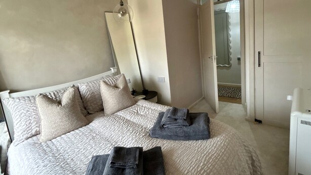 A modern bedroom with a large bed, a bedside table, a lamp, and a wardrobe. - Cosy Chichester Apartment (Chichester)
