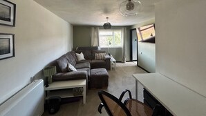 A compact living space with a sectional sofa, a dining table, and a ceiling light fixture. - Cosy Chichester Apartment (Chichester)