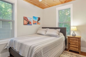 A bedroom with a bed, two wall-mounted pictures, a nightstand with a lamp, and a window with blinds.