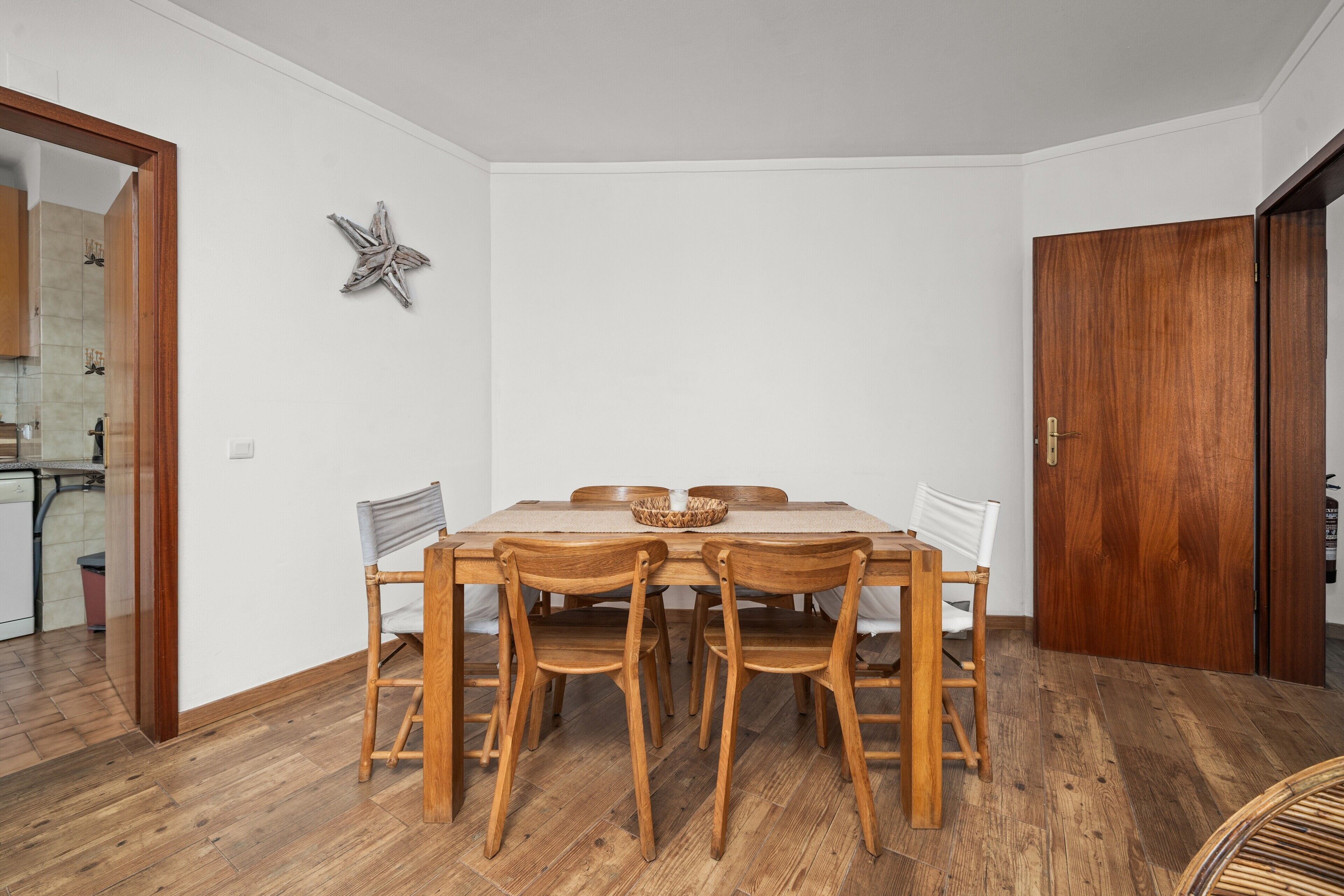 A dining area with a wooden table and chairs, a star decoration on the wall, and a wooden door.
