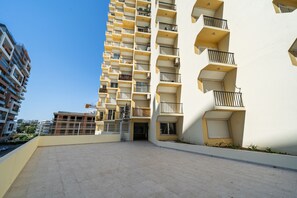 A multi-story residential building with balconies, a gated entrance, and a clear sky. - Apartment 'Rocha Beachside' with Balcony and Wi-Fi (Portimão)