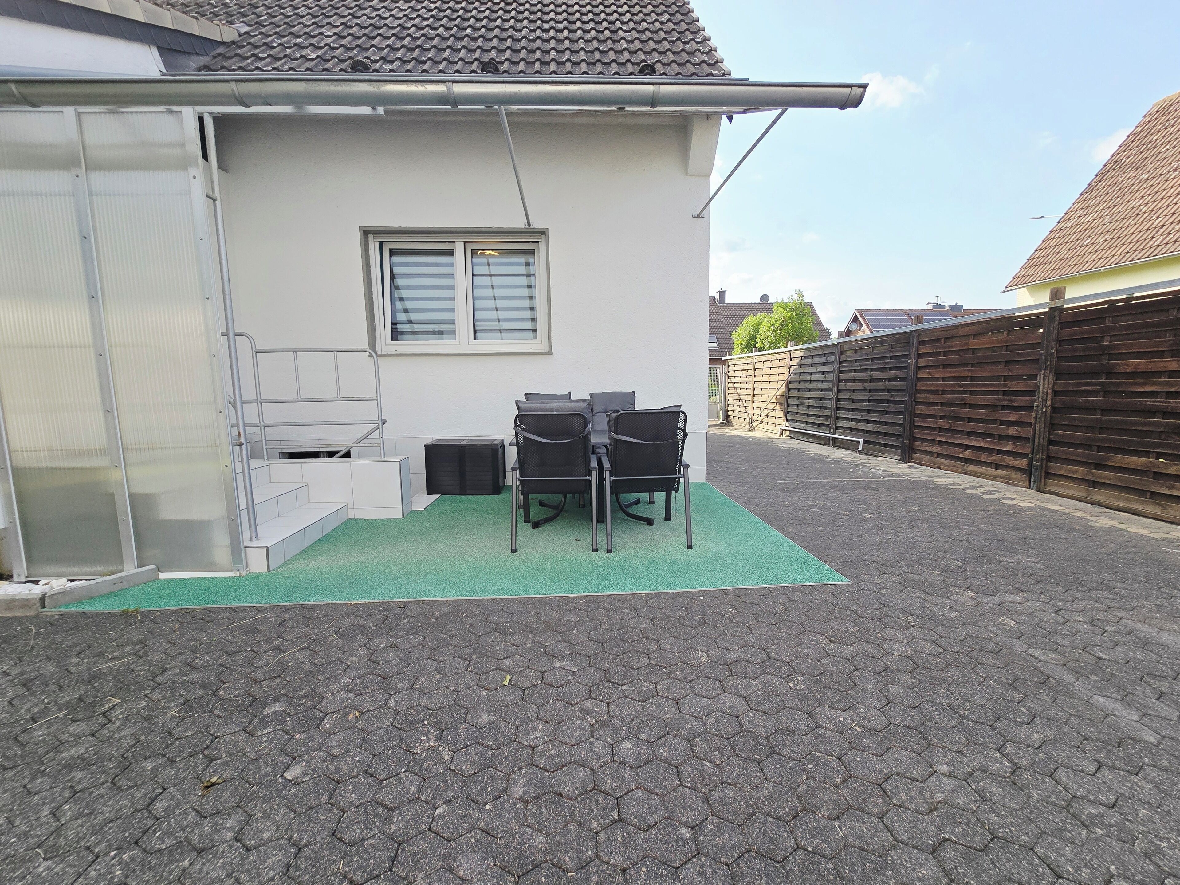 Un espace extérieur abrité, équipé d’une table et de chaises, d’une fenêtre et d’une clôture en bois.