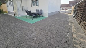 A patio with a table and chairs, a covered area, and a paved walkway.