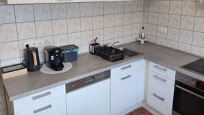 A modern kitchen with white cabinets, a built-in dishwasher, a coffee maker, and a stove.