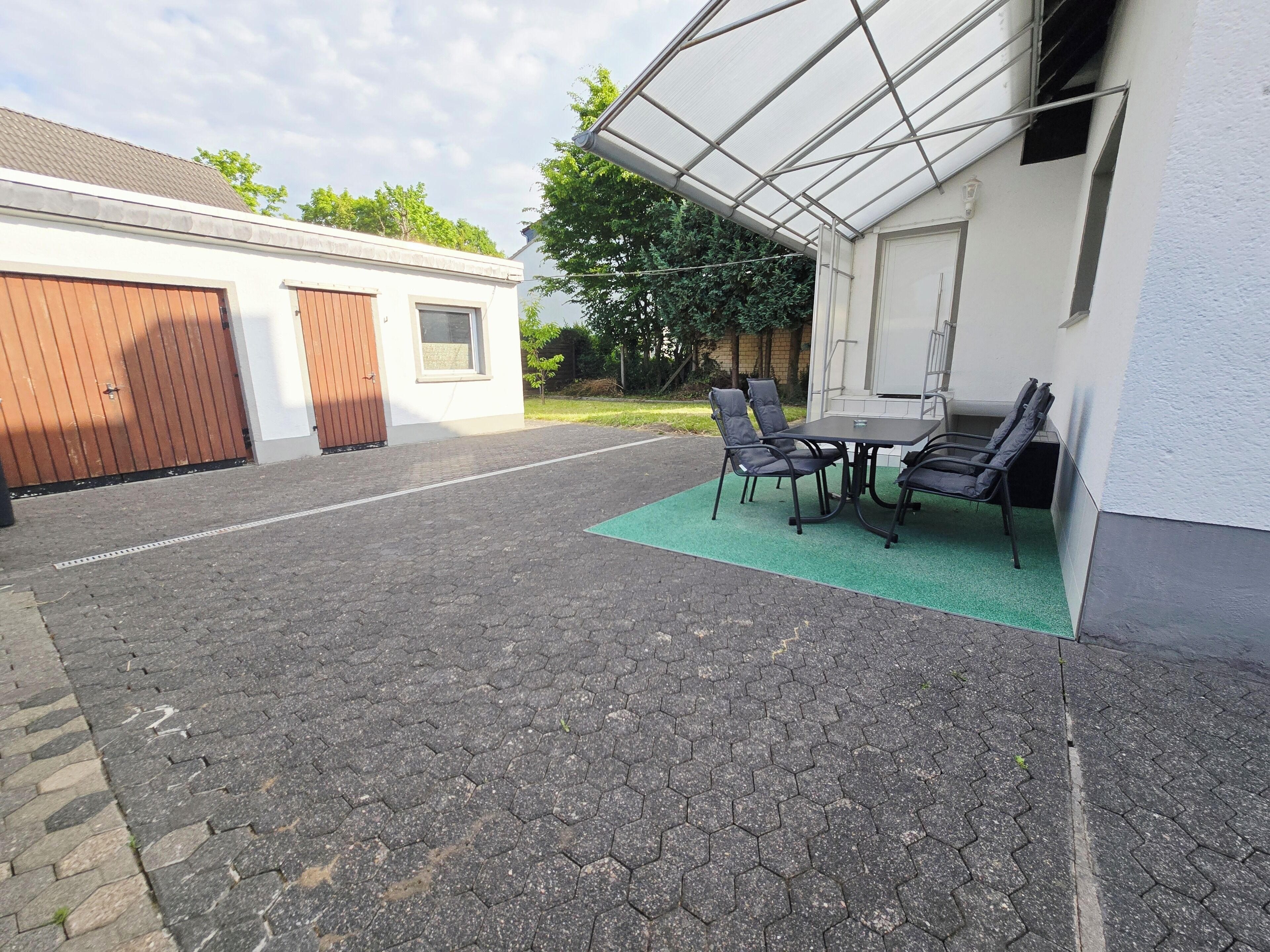A covered patio area with a table and chairs, a green mat, and a garage door.