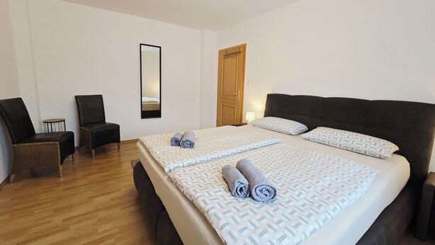 A hotel room with a large bed, two chairs, a small table, a mirror, and a wooden door.