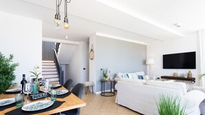 A modern living room with a sofa, a dining table set with plates and glasses, a TV mounted on the wall, and a staircase leading to another level. - Casa Uamisun with seaview & pool (Costa Adeje)