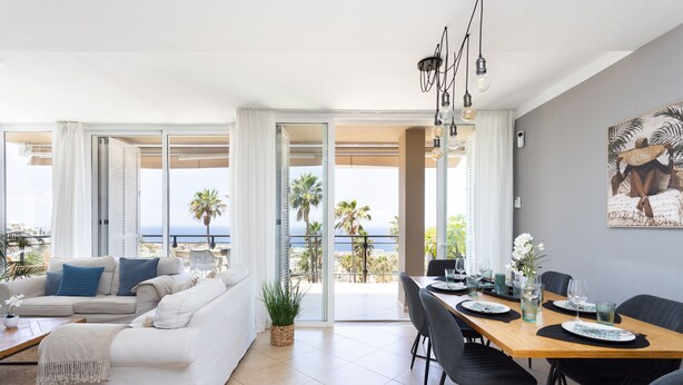 A modern living room with a sofa, dining table, and chairs, a balcony with a view of the sea, and a painting on the wall. - Casa Uamisun with seaview & pool (Costa Adeje)