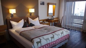 A hotel room with a large bed, two bedside lamps, a nightstand, a chair, and a window with sheer curtains. - Hotel Löwen (Reit im Winkl)