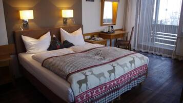 A hotel room with a large bed, two bedside lamps, a nightstand, a chair, and a window with sheer curtains.