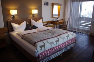 Una habitación de hotel con una cama grande, dos lámparas de noche, una mesita de noche, una silla y una ventana con cortinas traslúcidas.
