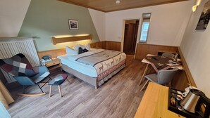 A bedroom with a bed, bedside table, chair, desk, and a kitchenette area. - Hotel Löwen (Reit im Winkl)