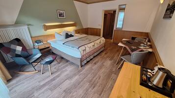 A bedroom with a bed, bedside table, chair, desk, and a kitchenette area.