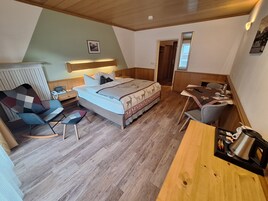 Un dormitorio con cama, mesita de noche, silla, escritorio y una zona de kitchenette.