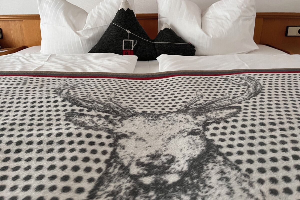A neatly made bed with white and black pillows, a patterned blanket, and a wooden headboard.