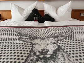 A neatly made bed with white and black pillows, a patterned blanket, and a wooden headboard.