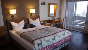 Une chambre d’hôtel avec un grand lit, deux lampes de chevet, une table de chevet, une chaise et une fenêtre avec des rideaux légers.
