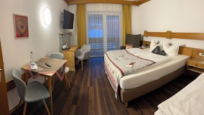 Une chambre d’hôtel comprenant un lit, un bureau avec une chaise, une télévision, une fenêtre avec des rideaux, ainsi qu’une petite table sur laquelle se trouvent une bouteille d’eau et une télécommande.