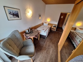 Una habitación acogedora con una cama, una silla, una mesita con un hervidor y tazas, y cuadros enmarcados en la pared.