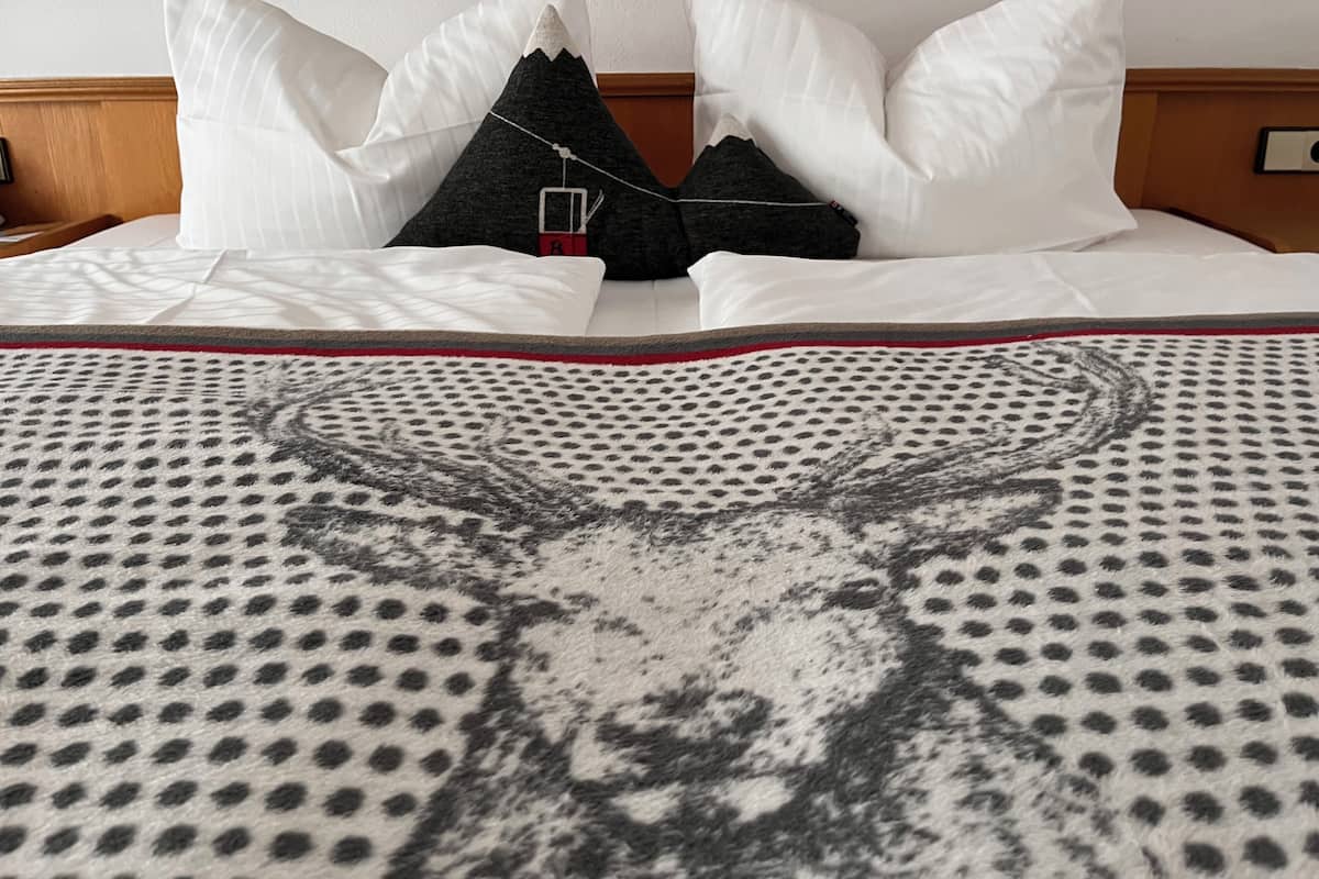 A neatly made bed with white and black pillows, a patterned blanket, and a wooden headboard.
