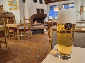 A glass of Löwenbräu beer in a cozy, rustic setting with wooden furniture and a fireplace.