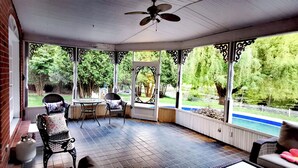 Eine überdachte Terrasse mit Deckenventilator, Blick auf den Pool und Gartenmöbeln.