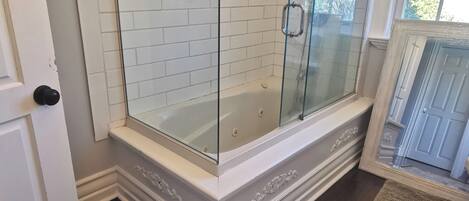Un baño con ducha de vidrio, paredes de azulejos blancos y suelo de madera.