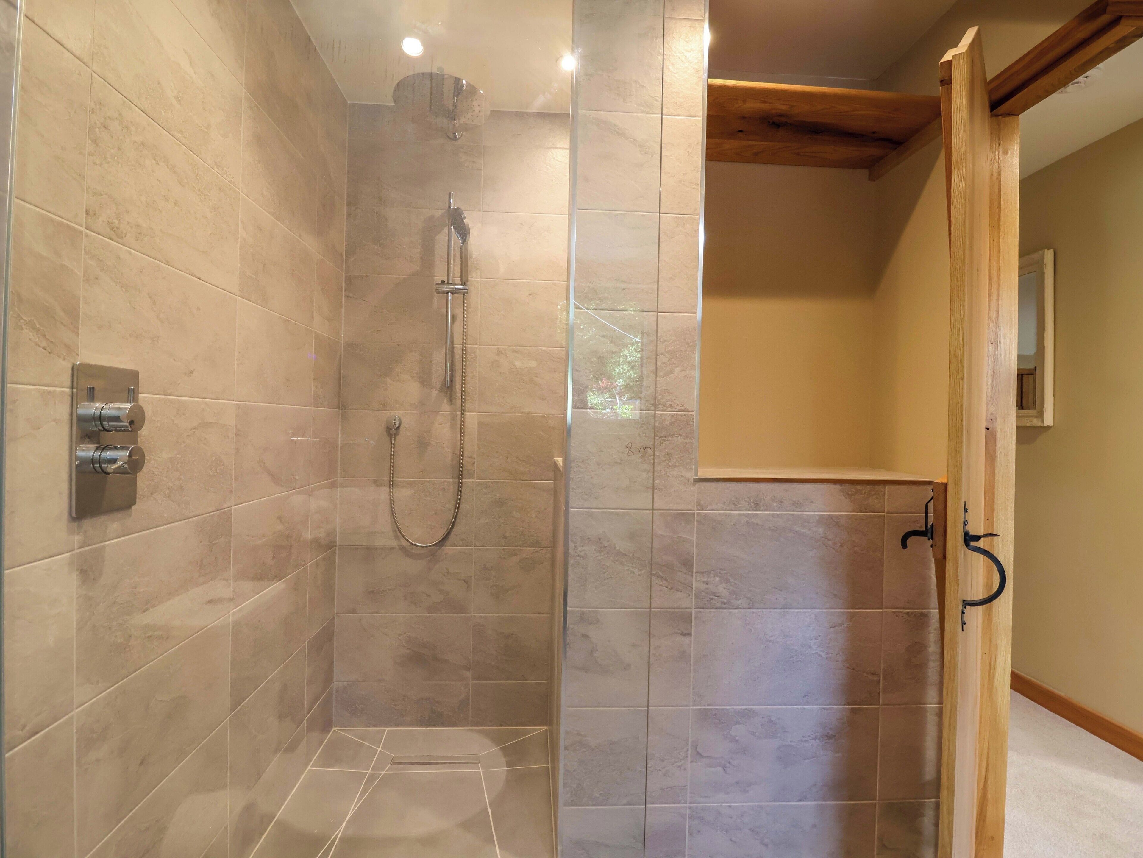 A walk-in shower with a glass door, tiled walls, and a wooden ceiling beam.