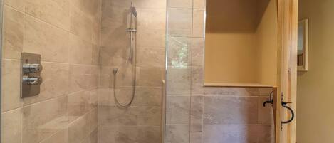 A walk-in shower with a glass door, tiled walls, and a wooden ceiling beam.