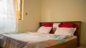 Ein Einzelbett mit Holzrahmen, roten und weißen Kissen und einer farbenfrohen Steude.