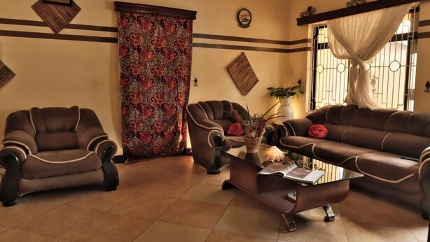 Un salón con un sofá marrón, dos sillones, una mesita de centro y una cortina estampada.