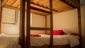 Una cama con dosel de madera con ropa de cama blanca y almohadas rojas, una ventana con barrotes de metal y un techo de madera.