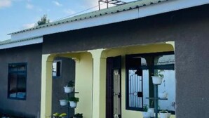 A building with a satellite dish, a covered porch with potted plants, and a concrete ground. - Msovi House - Standard Twin Room (Arusha)