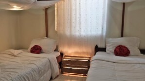 A bedroom with two beds, a wooden chest, and a window with sheer curtains. - Msovi House - Standard Twin Room (Arusha)