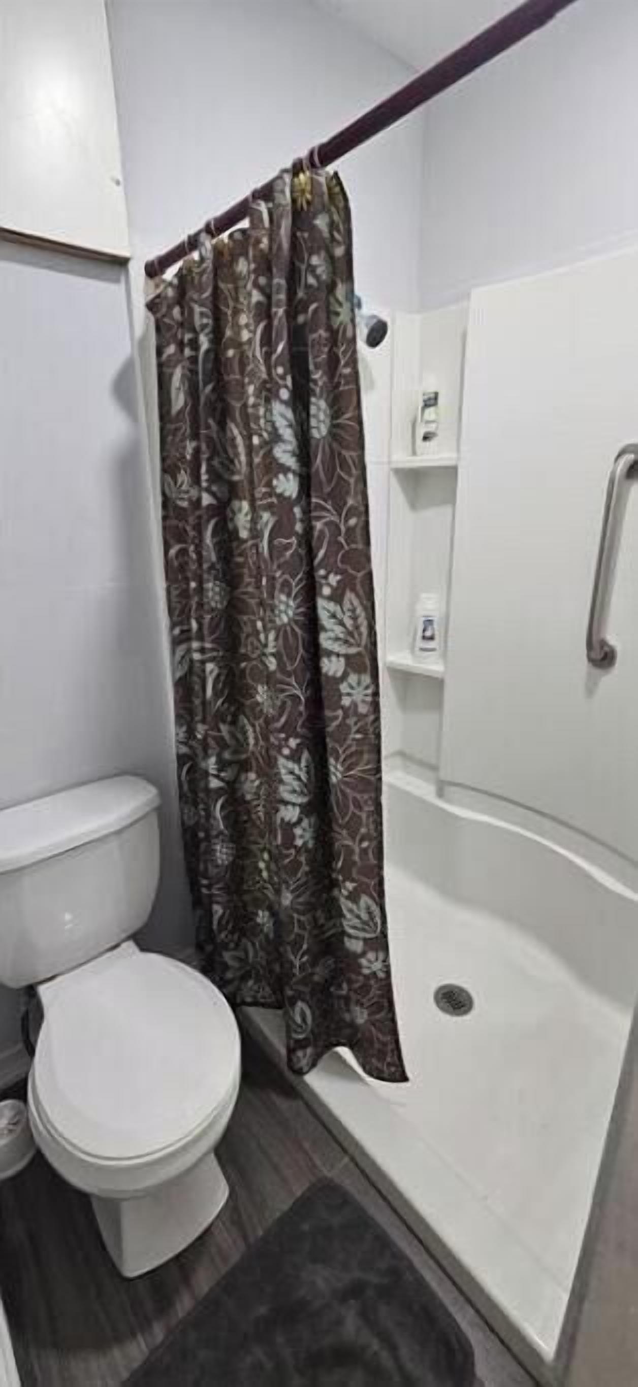 A bathroom with a toilet, a shower with a curtain, and a white bathtub.