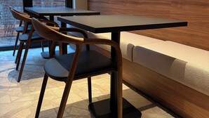 A modern dining area with wooden tables and chairs, a stone-patterned wall, and a view of a garden through large windows. - Door9 (Hasselt)