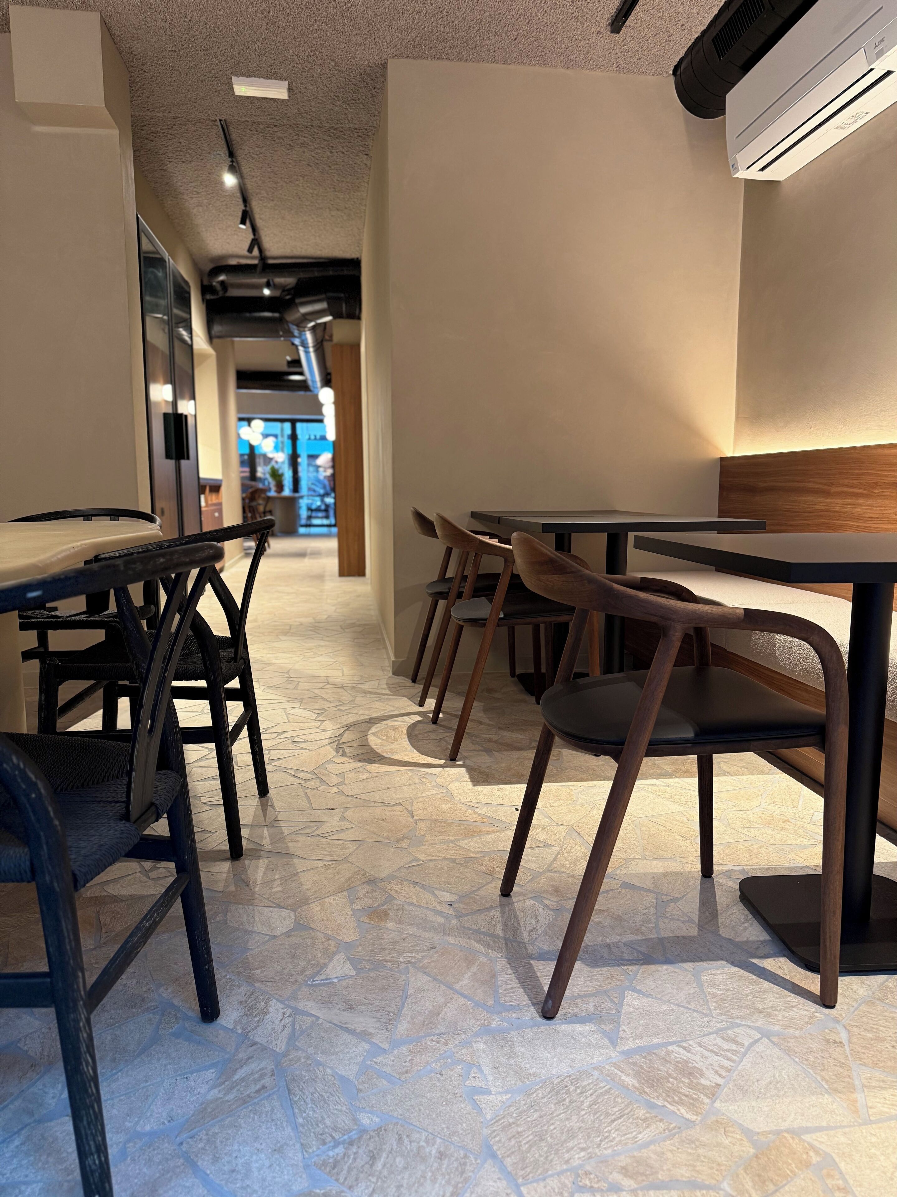 A modern interior with a mix of wooden and metal furniture, a patterned floor, and a ceiling with recessed lighting.