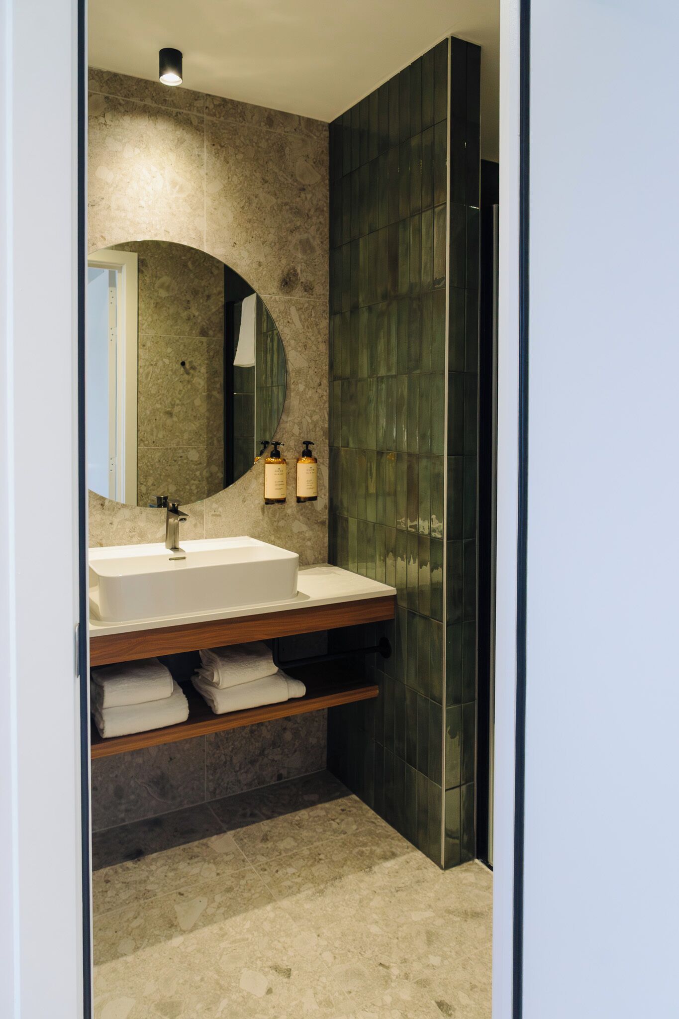Een moderne badkamer met een grote spiegel, een witte wastafel en twee flessen shampoo.