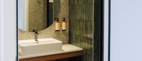 Un baño moderno con un espejo grande, un lavabo blanco y dos botellas de champú.