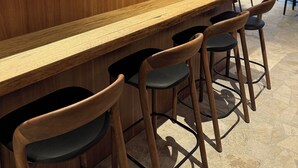 Eine Bar mit Holztresen, Barhocker und Regalen für Flaschen und Gläser.