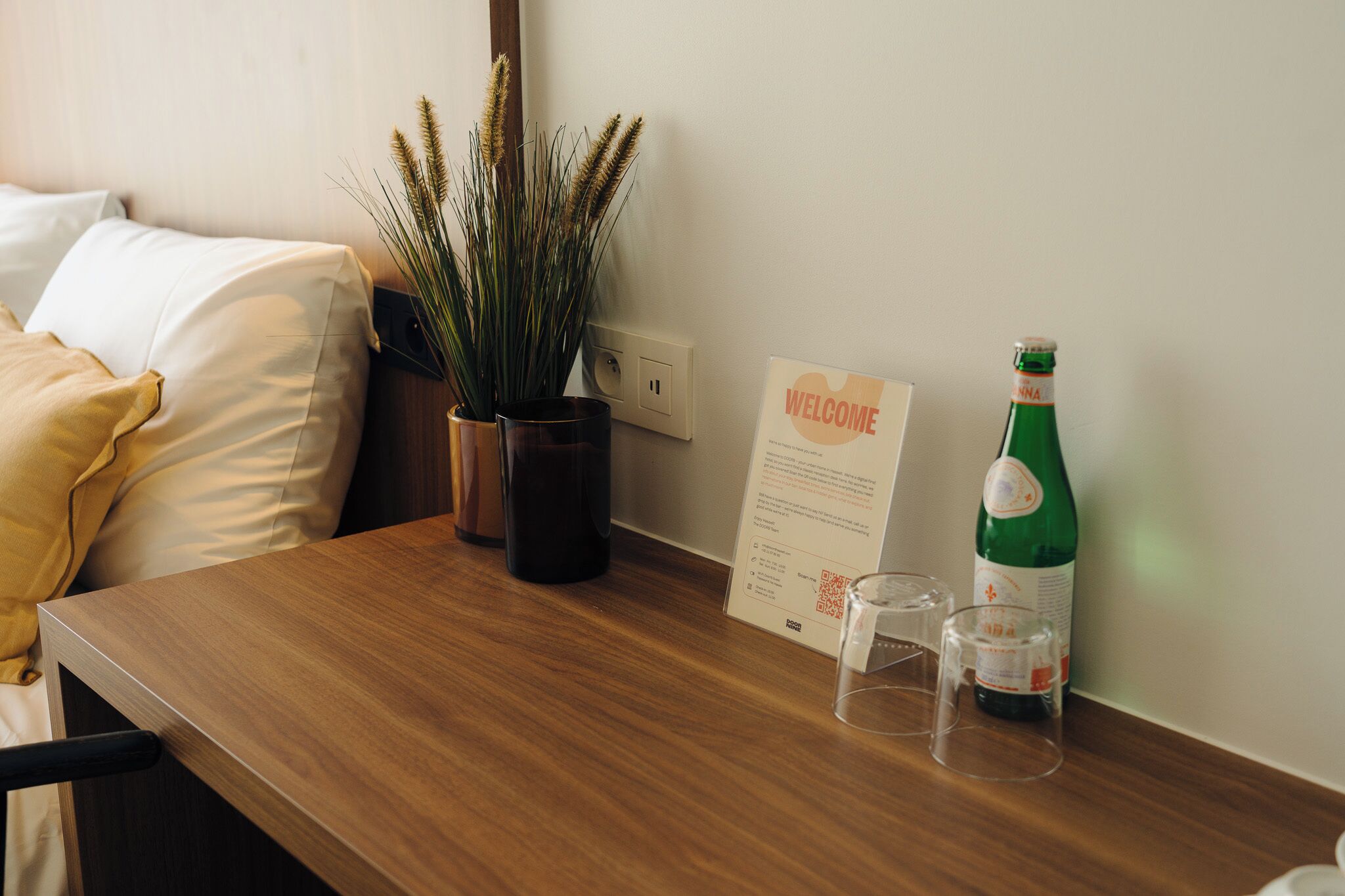 Una mesa de madera con un letrero de bienvenida, una botella verde y dos vasos.