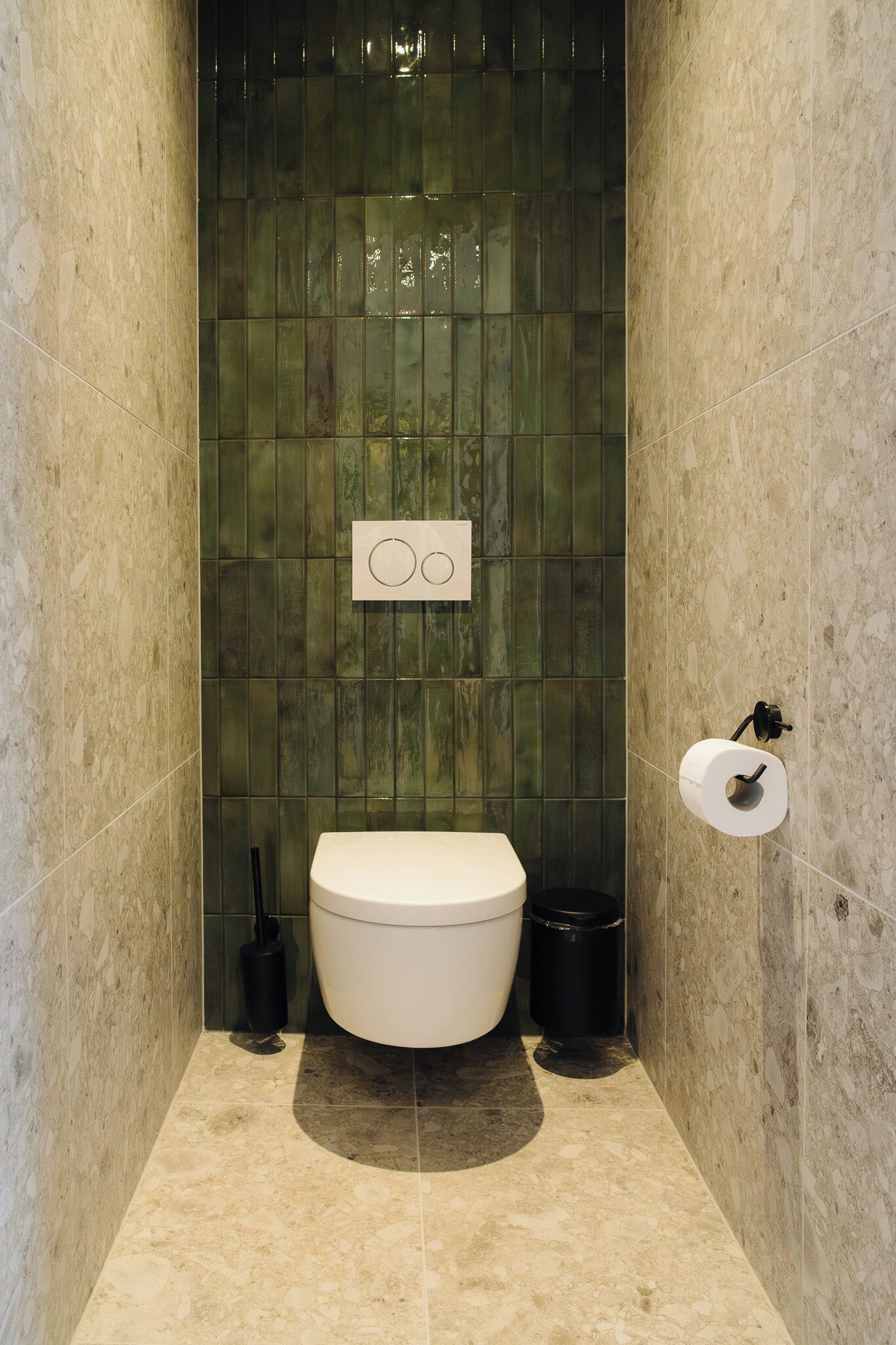 Een badkamer met een toilet, een prullenbak en een papieren handdoekdispenser.