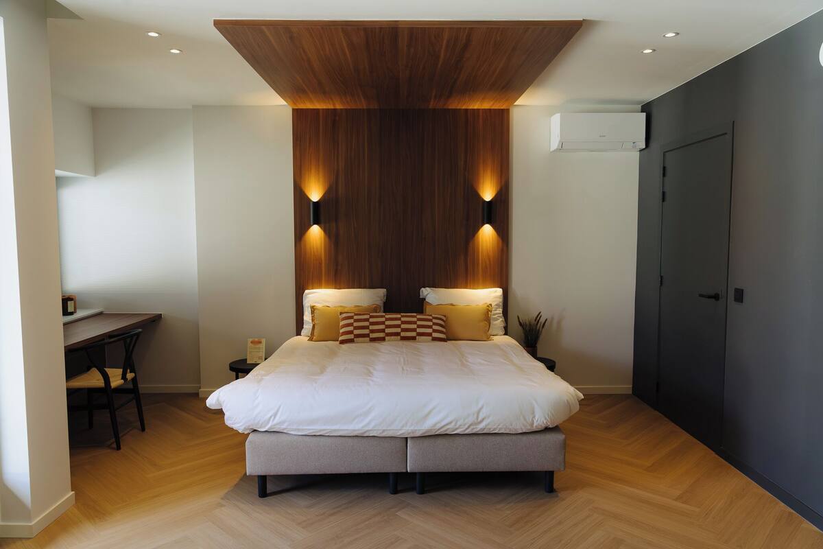 A modern bedroom with a large bed, two bedside lamps, a wooden ceiling, and a desk with a chair.