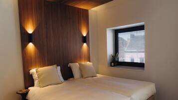 A bedroom with a large bed, two bedside tables, a wooden headboard, and a window with blinds.