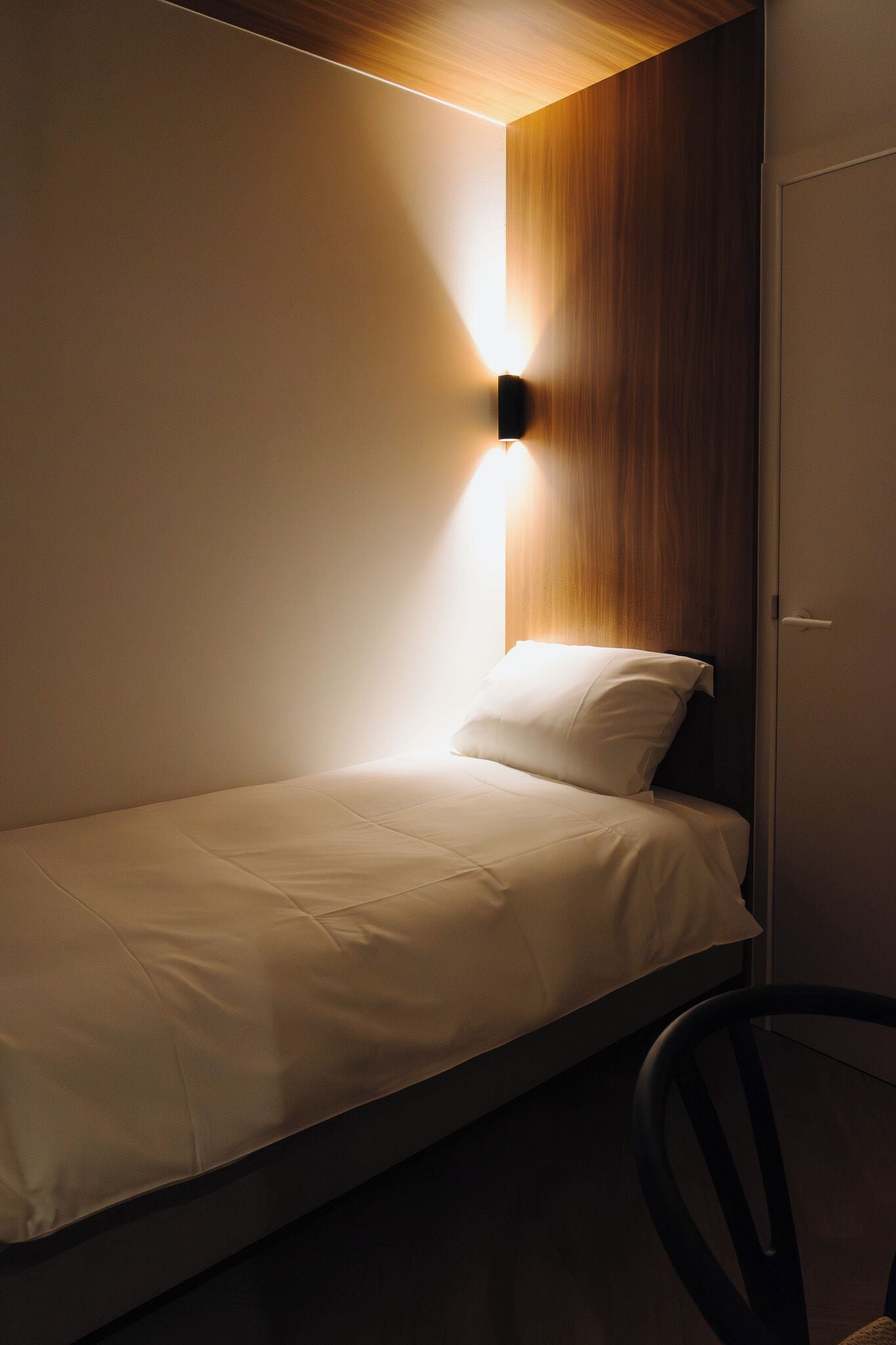 Un lit simple avec une tête de lit en bois et un luminaire fixé au mur.