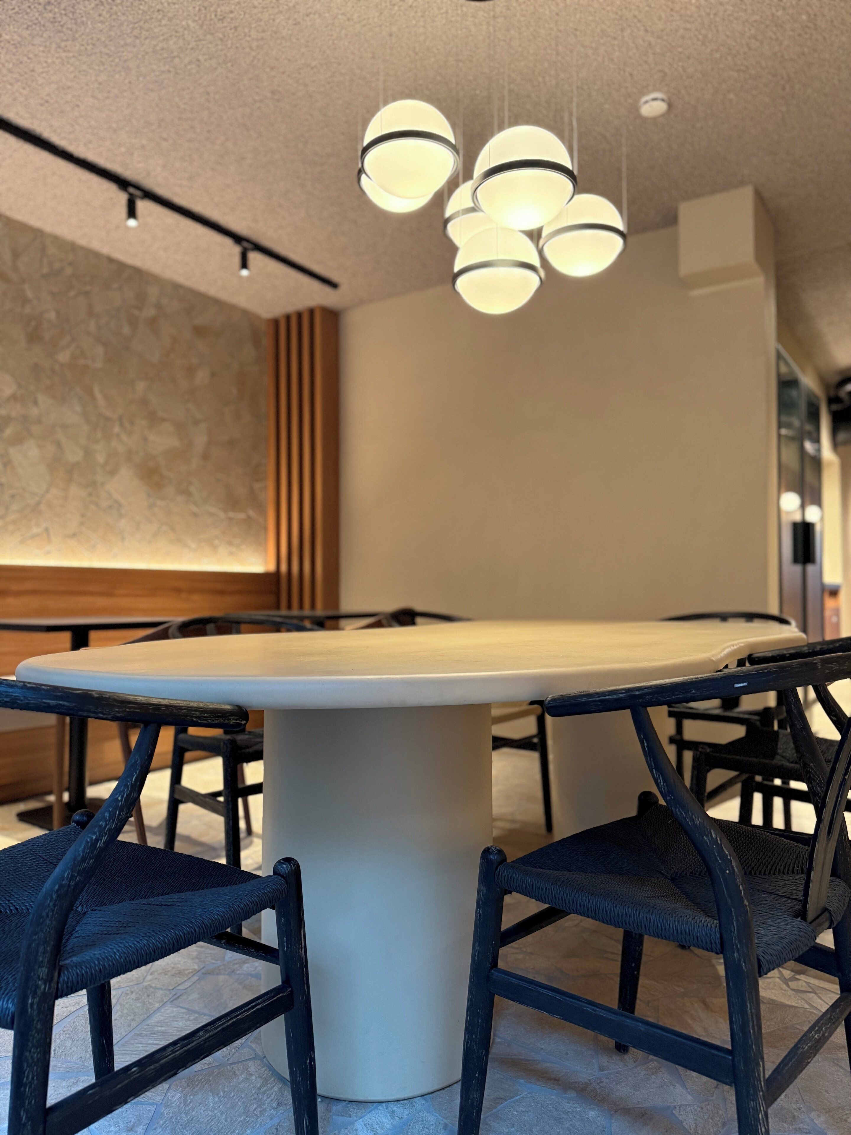 A conference room with a large oval table, black chairs, and a modern pendant light fixture.